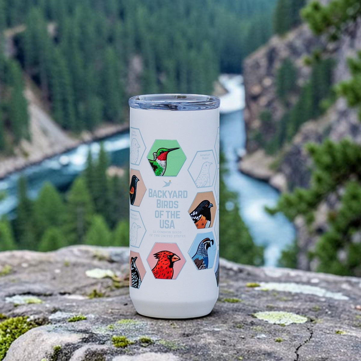 Beakwings white stainless steel tumbler featuring laser-engraved bird hexes and colorful bird stickers on a rock.